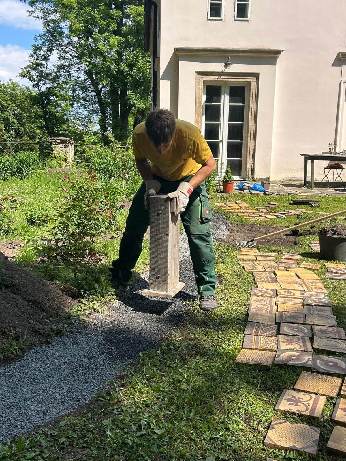 Zahradník pěchuje štěrkové lože rozdělané cesty