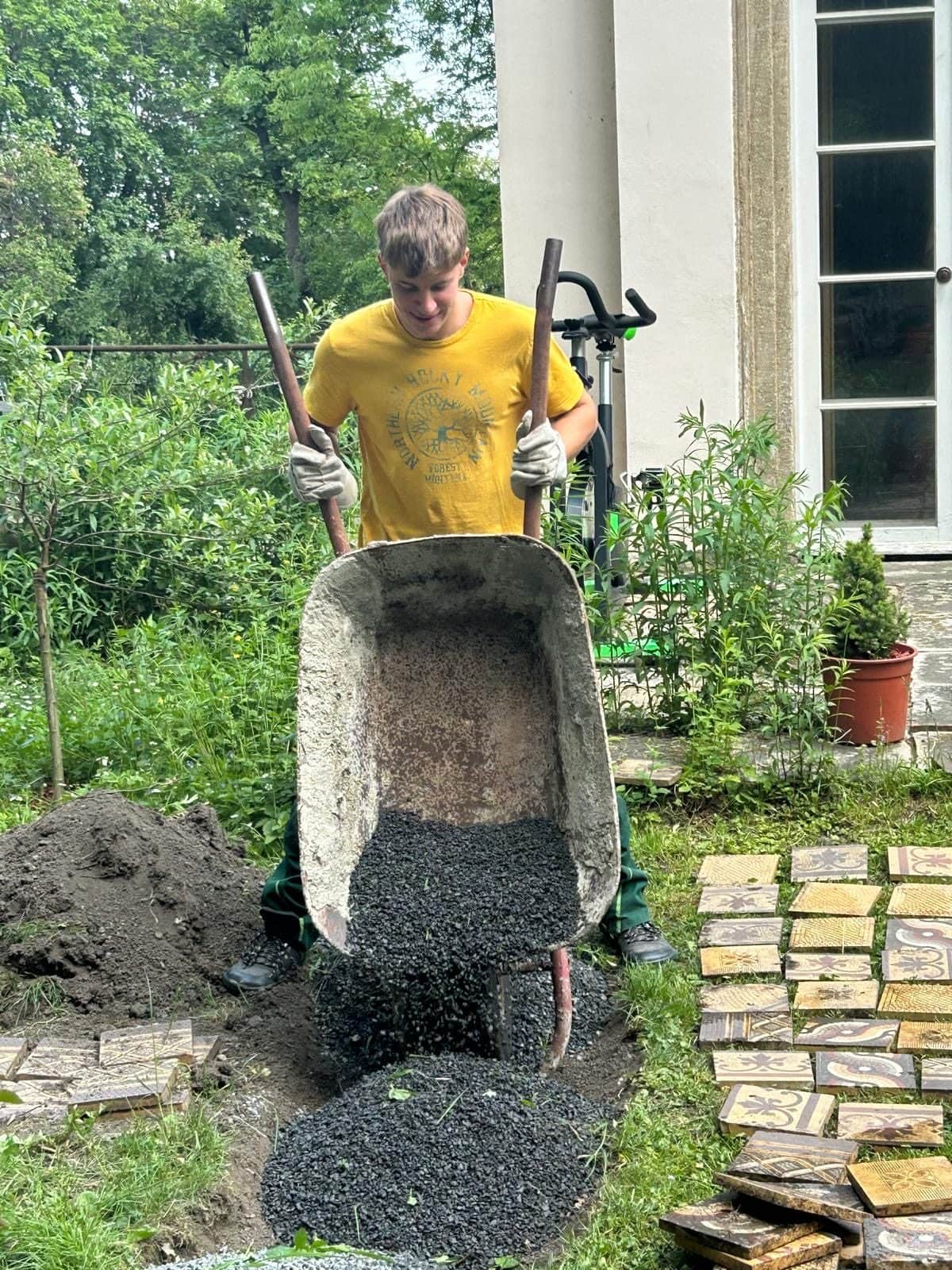 Zahradník vysypává kolečko se štěrkem vedle rozdělané cesty